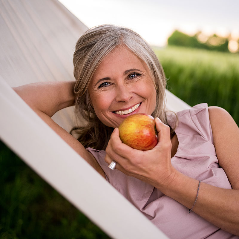 A lady holding a delicious apple while showing her dentures in a beautiful smile